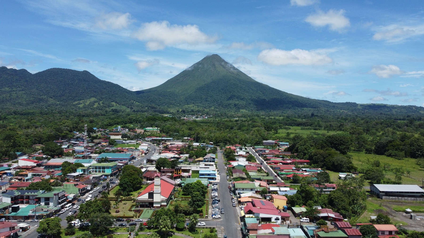 Drone view of La Fortuna with San Juan Bosco church, part of central park and Arenal Volcano in the background